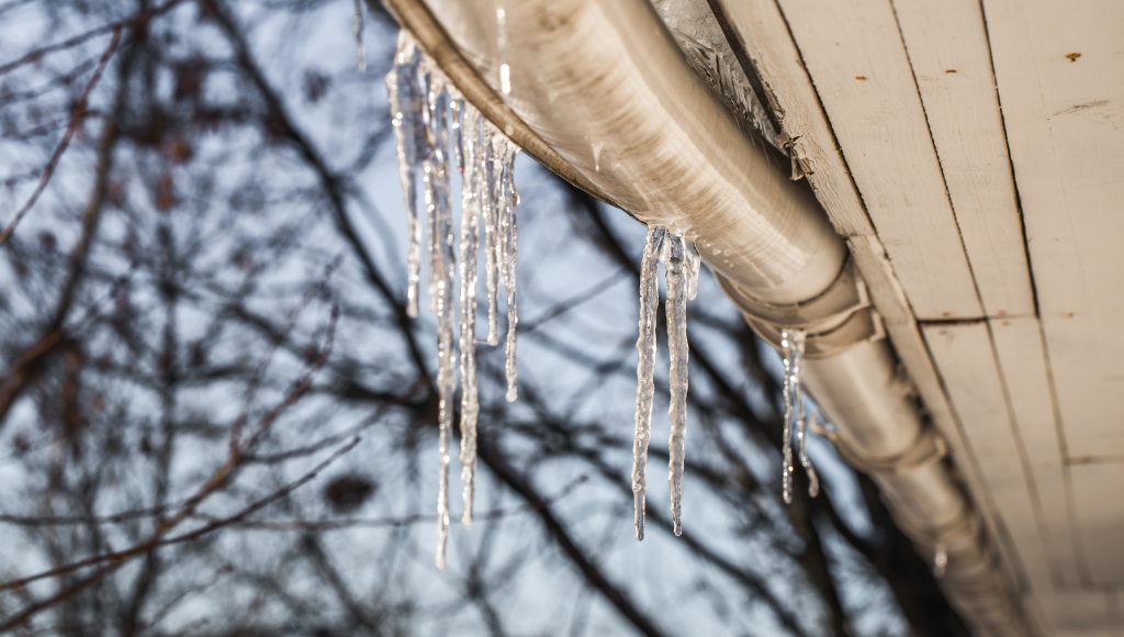 Icicles hanging from a gutter, causing it to pull away from the roof due to their weight.