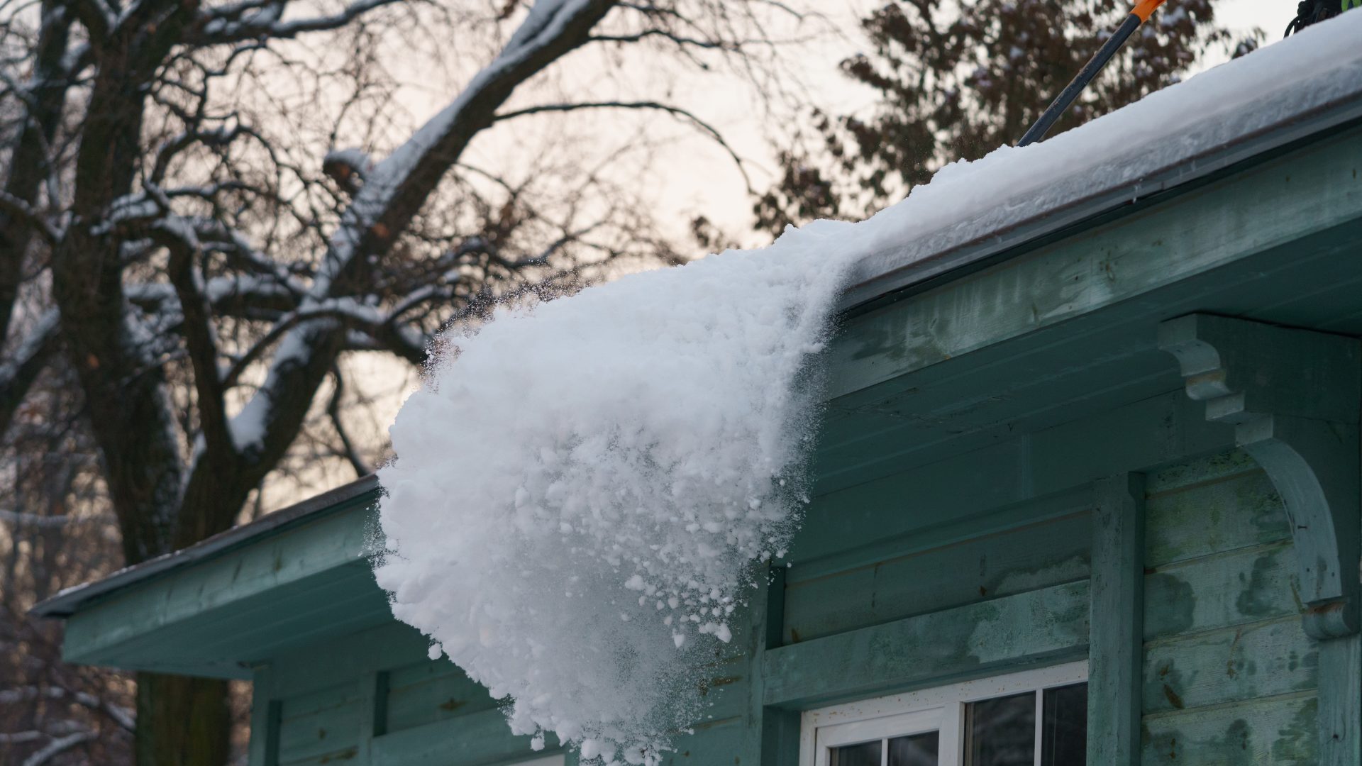 Someone shovelling snow off a roof for ice dam prevention after a storm.