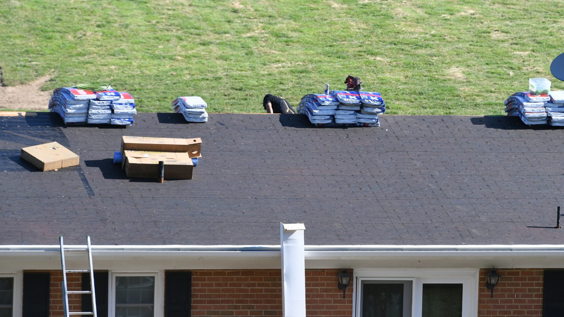 Roofers installing a new asphalt shingle roof on a red brick house.