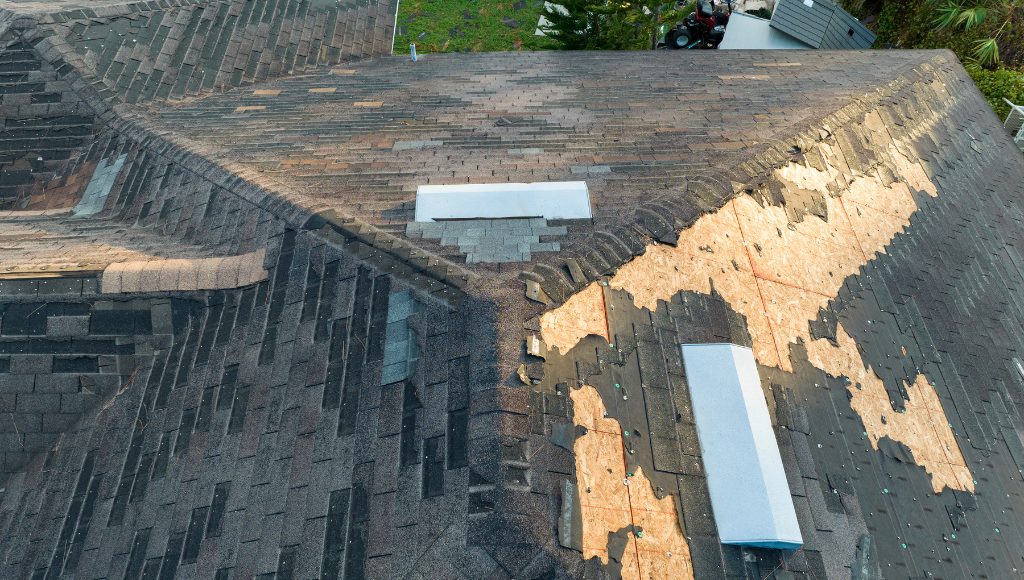 A wind-damaged roof with missing shingles and extensive granule loss.