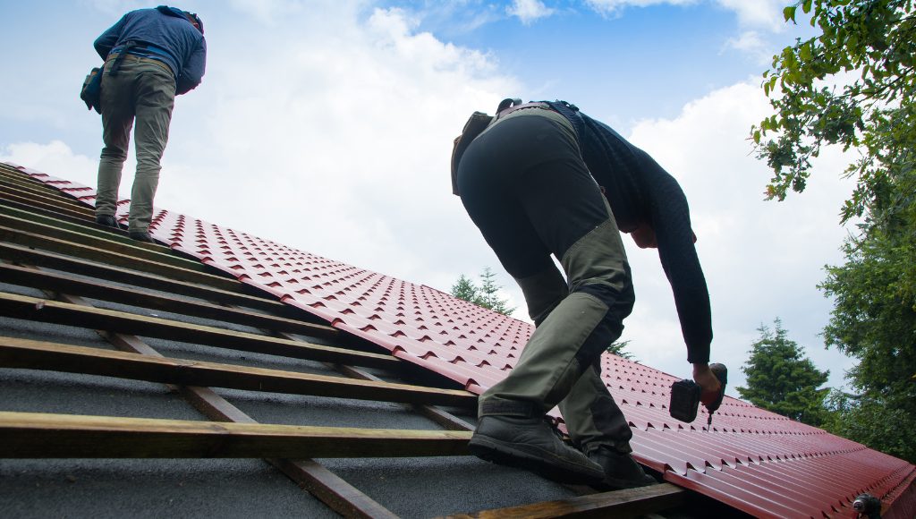 Roofers install a brand new red metal roof on a residential home.
